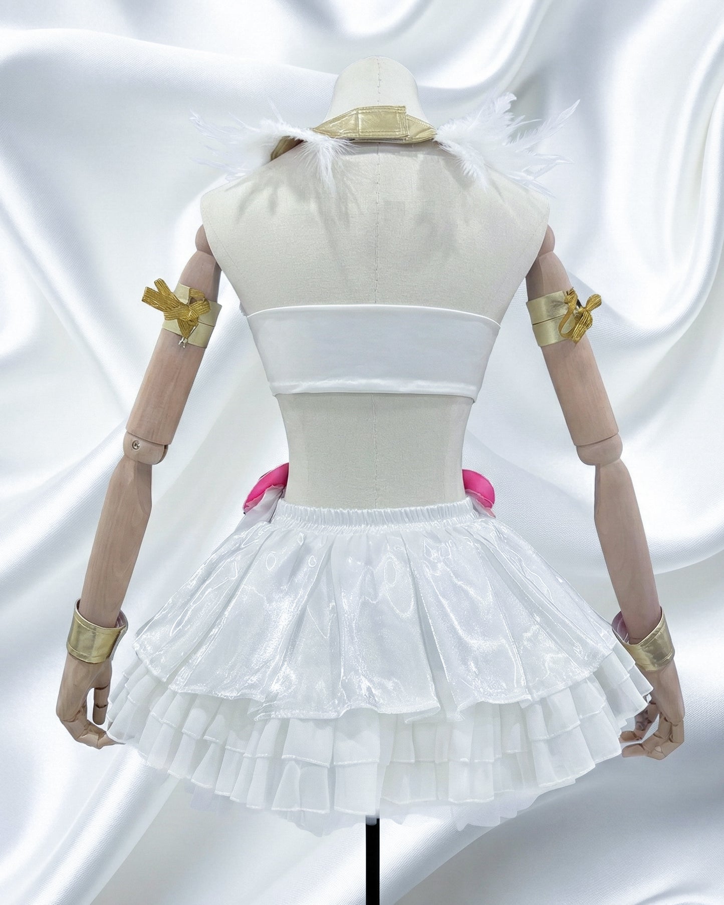 Rear view of the white angel cosplay outfit on a mannequin, highlighting the gold metallic arm bands, feathered shoulder pieces, and the volume of the tiered ruffled skirt.